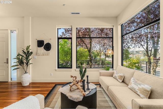 living room with baseboards, wood finished floors, visible vents, and a healthy amount of sunlight