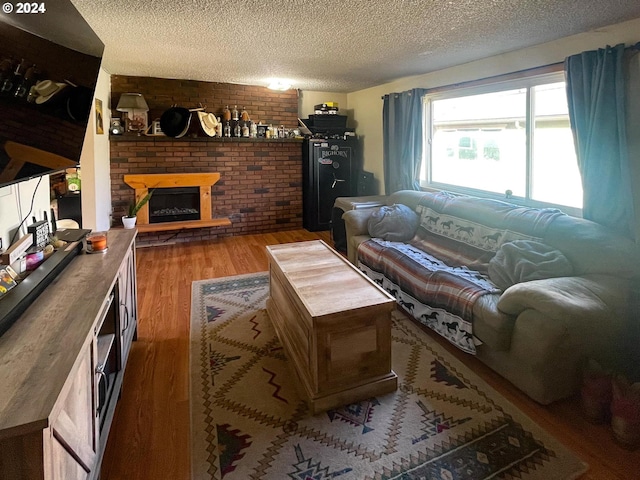 living room featuring wood-type flooring, a textured ceiling, and a brick fireplace