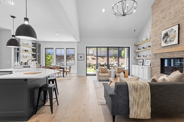 living room with a stone fireplace, a wealth of natural light, light hardwood / wood-style flooring, and an inviting chandelier