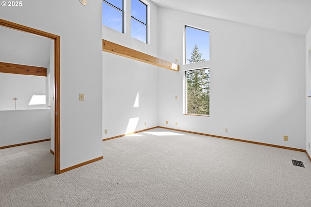 carpeted spare room featuring baseboards, visible vents, and a high ceiling