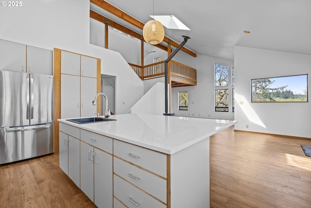 kitchen featuring freestanding refrigerator, a center island with sink, a sink, and lofted ceiling with skylight