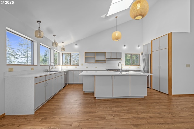 kitchen featuring a skylight, a center island with sink, a sink, high vaulted ceiling, and stainless steel appliances