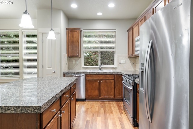 kitchen with stainless steel appliances, sink, light hardwood / wood-style floors, a kitchen island, and hanging light fixtures