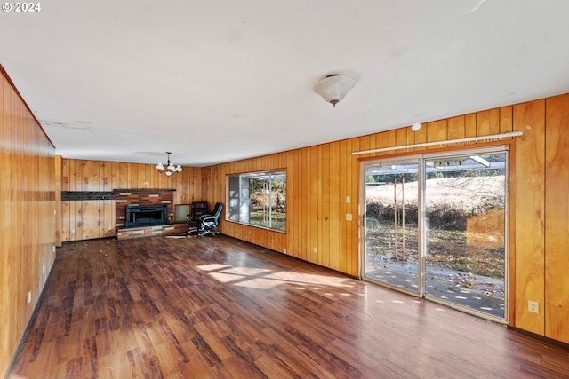 unfurnished living room with a brick fireplace, wood walls, a notable chandelier, and hardwood / wood-style flooring