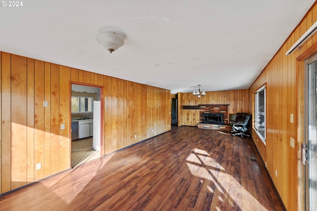 unfurnished living room with wood walls, an inviting chandelier, dark wood-type flooring, and a brick fireplace