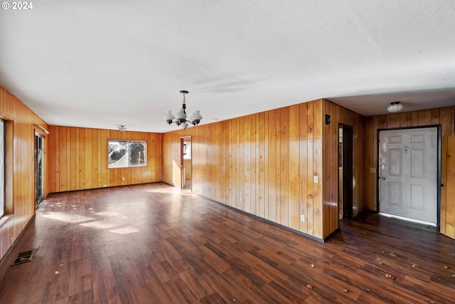 unfurnished living room with wood walls, a chandelier, and dark hardwood / wood-style floors