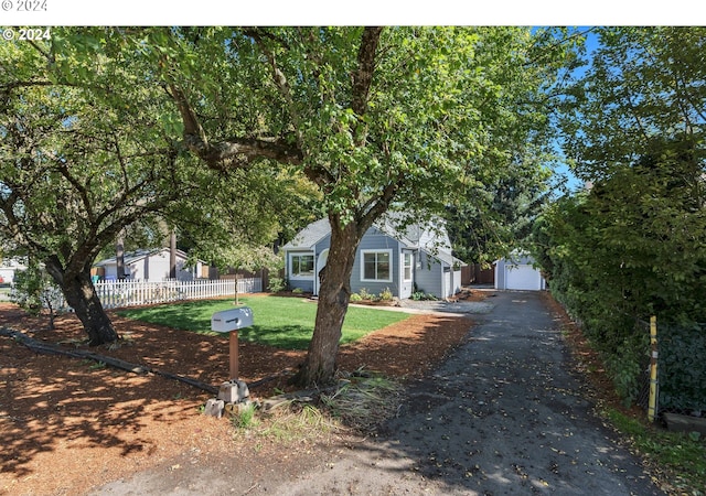 view of property hidden behind natural elements featuring a garage, a front lawn, and an outbuilding