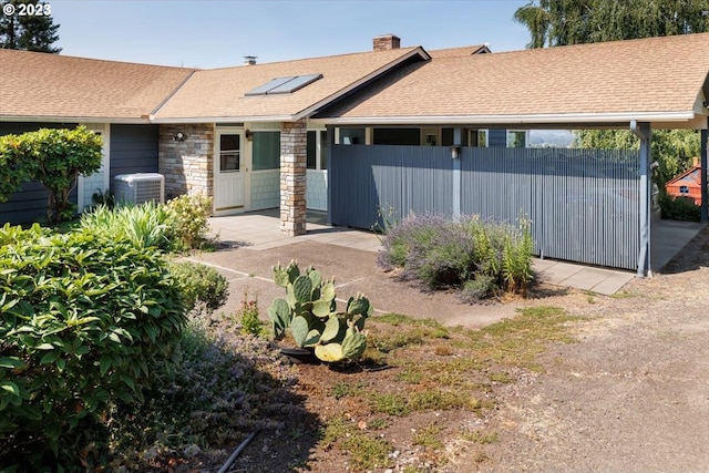 exterior space with a chimney, central air condition unit, a shingled roof, fence, and stone siding