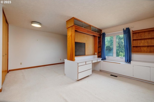 unfurnished living room featuring built in desk, a textured ceiling, and light carpet