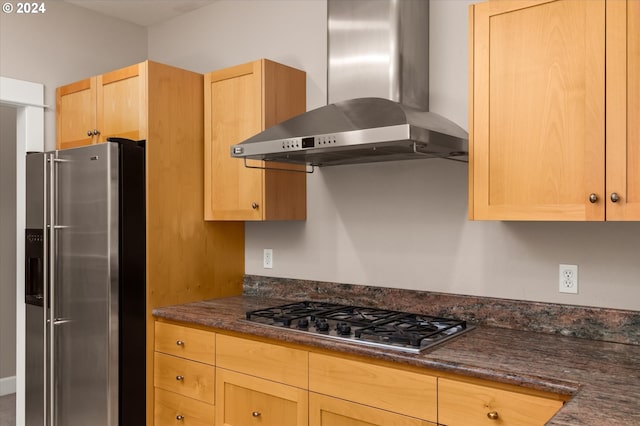 kitchen with stainless steel appliances, dark stone counters, light brown cabinets, and wall chimney range hood