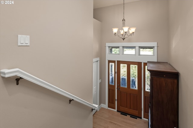 foyer entrance featuring a towering ceiling, a notable chandelier, and light wood-type flooring