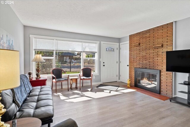 living room with a textured ceiling, a brick fireplace, and hardwood / wood-style floors