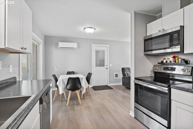 kitchen with light wood-type flooring, a wall mounted air conditioner, white cabinetry, sink, and appliances with stainless steel finishes