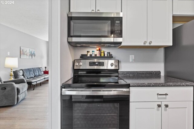 kitchen with light wood-type flooring, appliances with stainless steel finishes, vaulted ceiling, and white cabinets