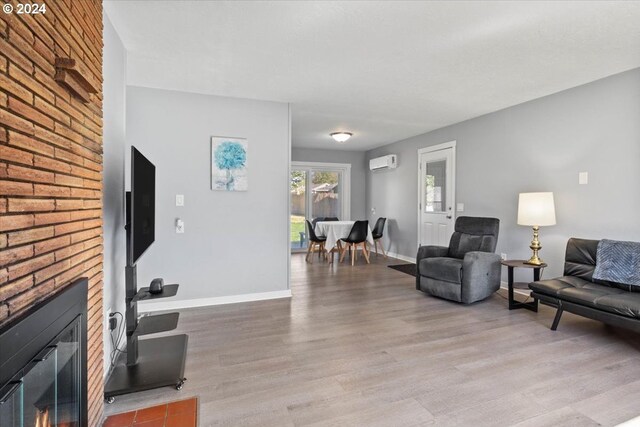 living room with a wall unit AC, a brick fireplace, and hardwood / wood-style flooring