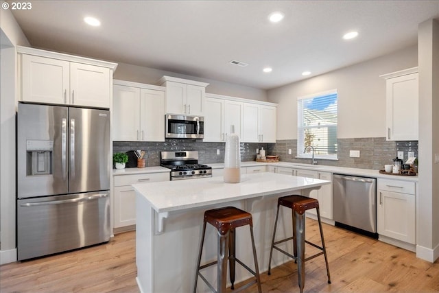 kitchen with a kitchen island, appliances with stainless steel finishes, white cabinetry, and light hardwood / wood-style floors