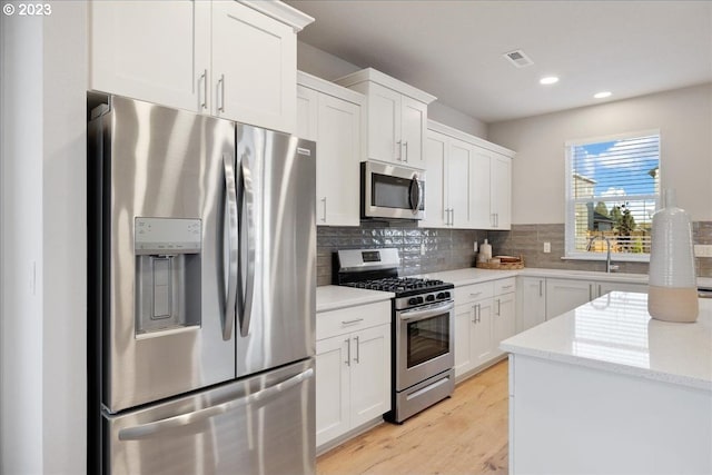 kitchen featuring light hardwood / wood-style flooring, stainless steel appliances, light stone countertops, white cabinetry, and tasteful backsplash