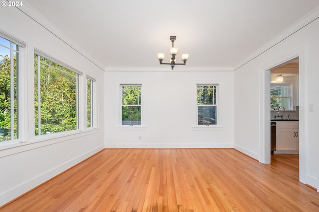 spare room with light hardwood / wood-style flooring, a wealth of natural light, a chandelier, and crown molding