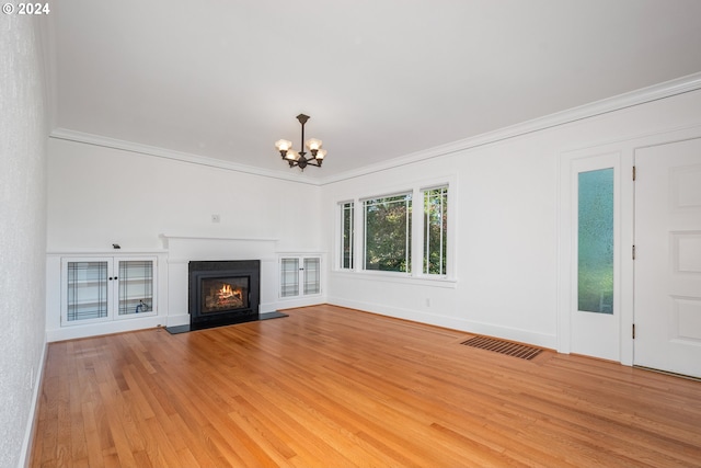 unfurnished living room featuring an inviting chandelier, hardwood / wood-style flooring, and crown molding