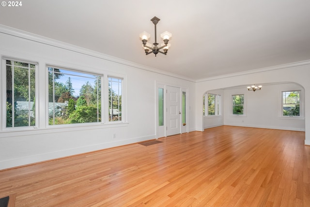 unfurnished living room with an inviting chandelier, crown molding, and light hardwood / wood-style floors