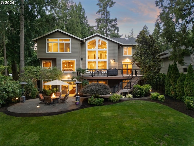 back of house at dusk with a wooden deck, stairs, a lawn, a patio area, and driveway