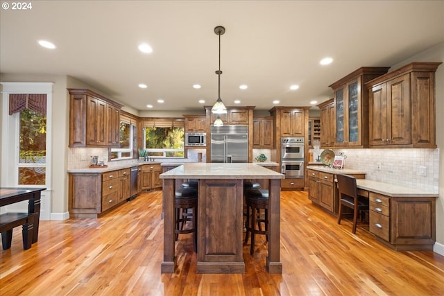 kitchen with light stone counters, a center island, brown cabinets, hanging light fixtures, and built in appliances