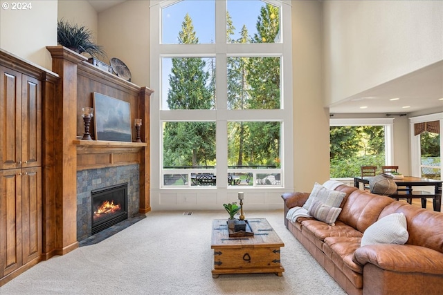 living room featuring a fireplace with flush hearth, light carpet, and a towering ceiling