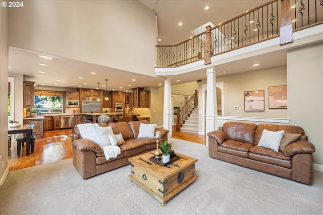 living area featuring light wood-type flooring, decorative columns, stairs, and a towering ceiling