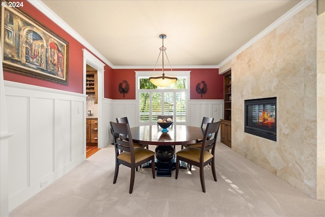 dining space featuring a decorative wall, light carpet, a fireplace, ornamental molding, and wainscoting