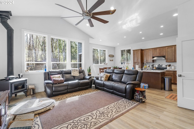 living room featuring ceiling fan, a wood stove, light hardwood / wood-style flooring, and vaulted ceiling