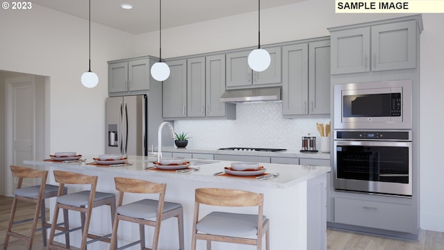 kitchen with a breakfast bar, a center island with sink, pendant lighting, and appliances with stainless steel finishes