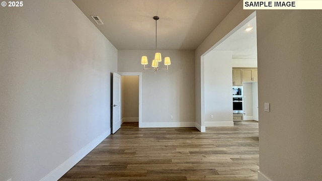 unfurnished dining area featuring baseboards, a chandelier, wood finished floors, and visible vents