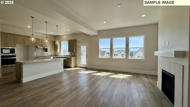 kitchen featuring under cabinet range hood, stainless steel appliances, light countertops, dark wood-type flooring, and decorative backsplash