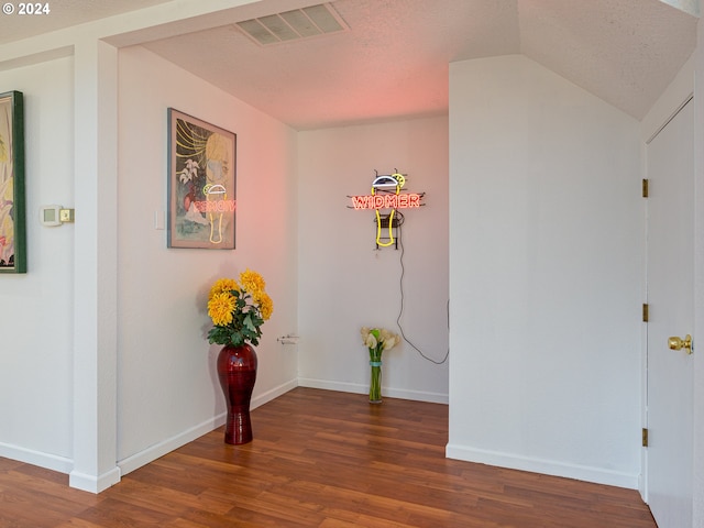 corridor with lofted ceiling, a textured ceiling, and dark wood-type flooring