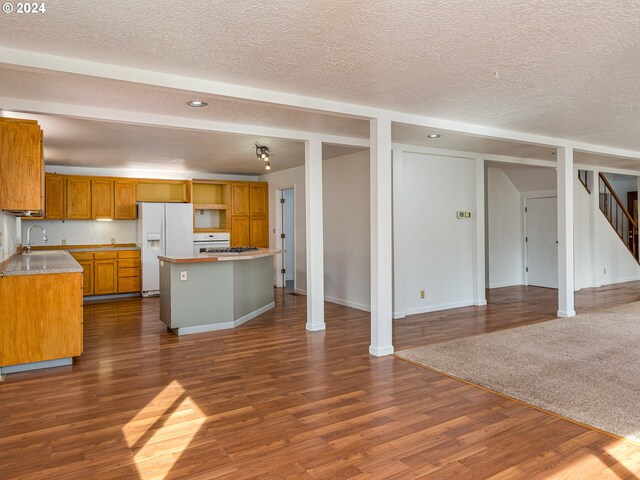 kitchen with white appliances, a textured ceiling, a center island, and dark wood-type flooring