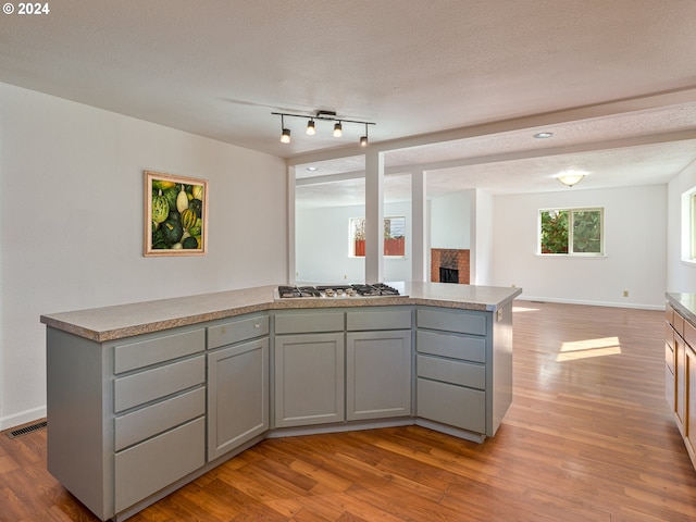 kitchen featuring stainless steel gas stovetop, light wood-type flooring, a textured ceiling, and a fireplace