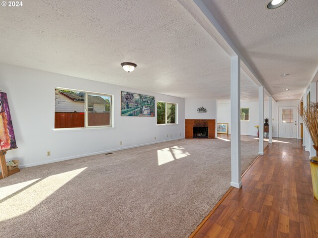 unfurnished living room featuring a brick fireplace, a textured ceiling, and dark wood-type flooring