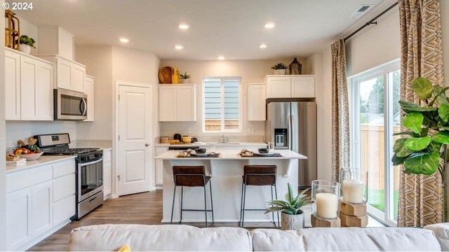 kitchen featuring a kitchen island, white cabinetry, light wood-type flooring, a kitchen breakfast bar, and stainless steel appliances