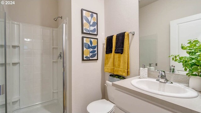 bathroom featuring toilet, vanity, decorative backsplash, and a shower with door