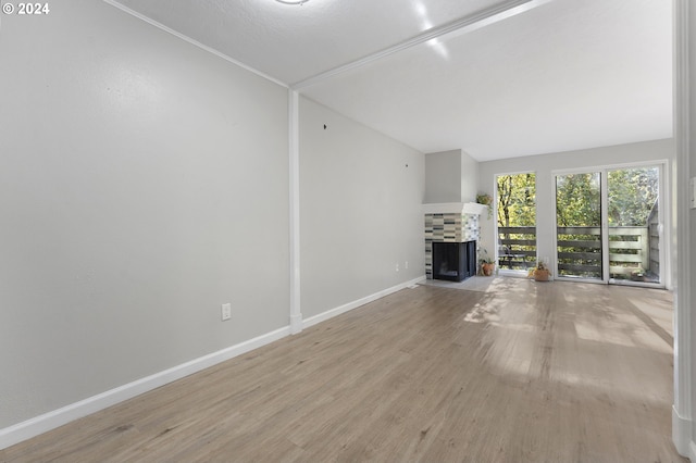 unfurnished living room featuring a tile fireplace, lofted ceiling, and light wood-type flooring