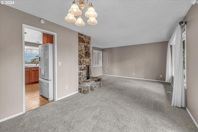 unfurnished living room featuring a fireplace, a chandelier, light carpet, and a textured ceiling