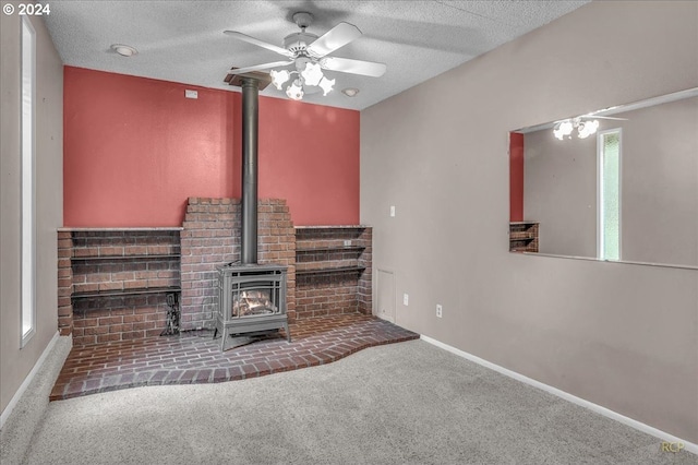 unfurnished living room with ceiling fan, a wood stove, a textured ceiling, and carpet floors