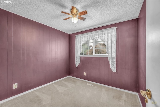 carpeted empty room featuring a textured ceiling, ceiling fan, and wooden walls