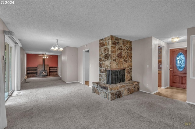 unfurnished living room featuring a textured ceiling, ceiling fan with notable chandelier, carpet floors, and a fireplace