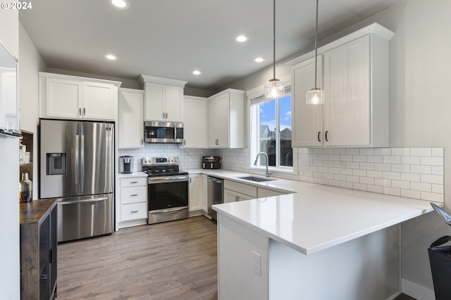 kitchen with white cabinetry, sink, kitchen peninsula, decorative light fixtures, and appliances with stainless steel finishes