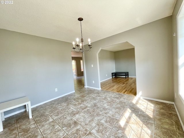 tiled spare room with a textured ceiling and an inviting chandelier