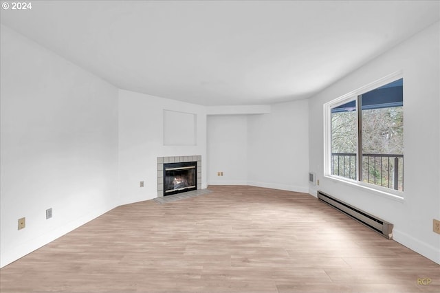 unfurnished living room with light hardwood / wood-style floors, baseboard heating, and a tiled fireplace