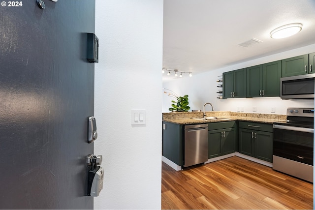 kitchen featuring appliances with stainless steel finishes, light hardwood / wood-style floors, sink, green cabinets, and rail lighting