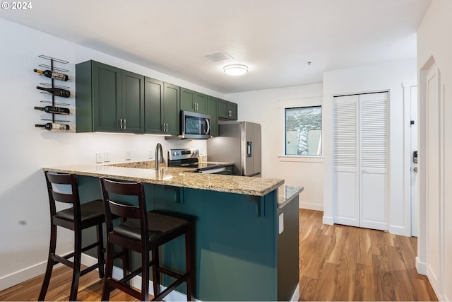 kitchen featuring light hardwood / wood-style floors, a kitchen bar, appliances with stainless steel finishes, and light stone counters