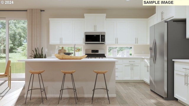 kitchen with a kitchen breakfast bar, stainless steel appliances, white cabinetry, light hardwood / wood-style floors, and a kitchen island